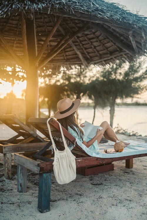Guest reading under a thatched umbrella on the sand at golden hour